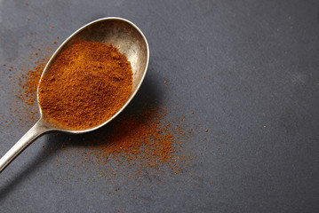 An antique silver spoon full of chili powder seasoning on a rustic slate background forming a page border