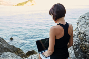 Beautiful young freelancer woman using laptop sitting near the sea.Happy smiling girl working online.Studying and learning using notebook computer.Freelance work,business people concept.