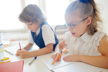 Cute little schoolgirl in glasses something diligently writes in a copybook.