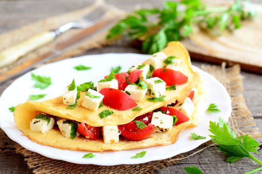 Stuffed omelette on a plate. Fried omelette stuffed with cheese, tomatoes and parsley. Breakfast recipe. Closeup