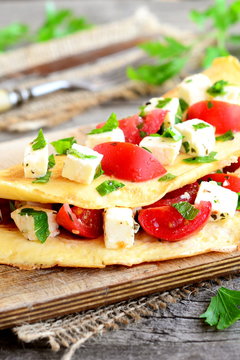 Stuffed omelette on a wooden board. Fried omelet stuffed with cheese, tomatoes and parsley. Eggs recipe. Closeup