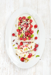 Homemade semifreddo with pistachio and raspberry in oval dish over old white painted wooden background, top view
