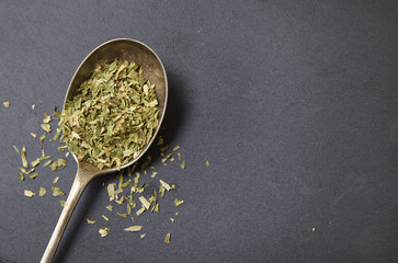 An antique spoon full of the seasoning tarragon, on a rustic slate background forming a page border