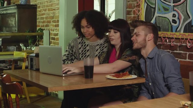 Three friends browsing on laptop at pizza place - 4K