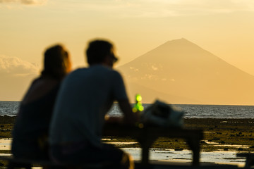 Tourists in the restaurant on Gili Travangan island enjoying evening sunset view on Gunung Batur volcano on Bali, Indonesia.