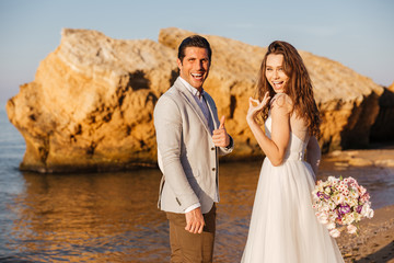 Just-married couple walking at beach and showing ok sign