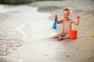 Happy child playing with sand at the beach in summer