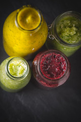 Bottles and jar with different smoothie on the dark stone table vertical