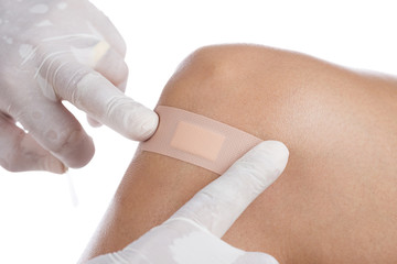 Hands of a doctor applying adhesive bandage on knee of a caucasian woman isolated 