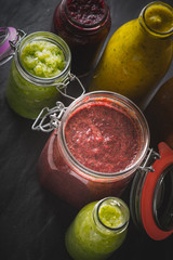 Jars and bottles with different smoothie on the dark stone table