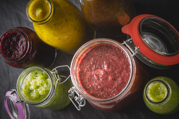 Jars and bottles with different smoothie on the dark stone table  horizontal
