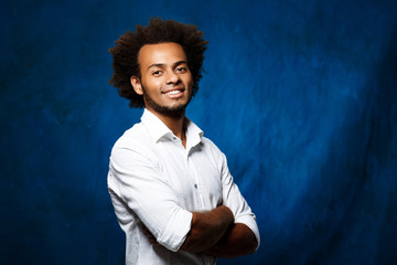 Young handsome african man with crossed arms over blue background.