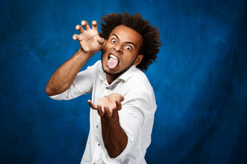 Young handsome african man showing tongue, fooling over blue background.