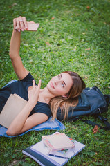 happy girl student lying on the grass in the park and makes selfi