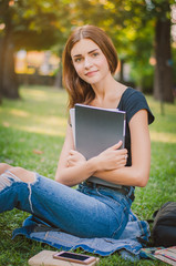 Fototapeta premium happy girl student sitting on the grass with books in their hand
