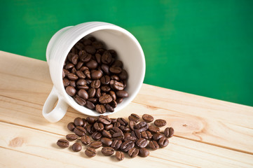 coffee beans spilled from cup on pine wood table with nature green background