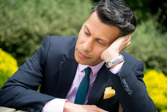 Frustrated businessman sitting at a table resting his head against his hand.