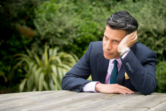 Frustrated businessman sitting at a table resting his head against his hand.