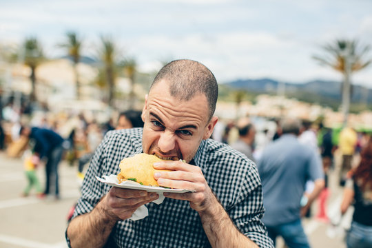 Man bites a hamburger and looking to the camera