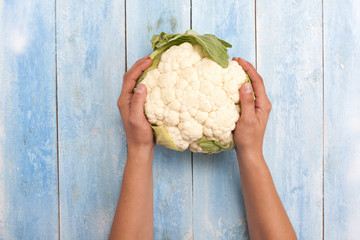 Cauliflower in hands with blue wooden board in background, top view