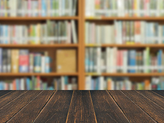 Wooden desk space and blurred book shelf in library room background