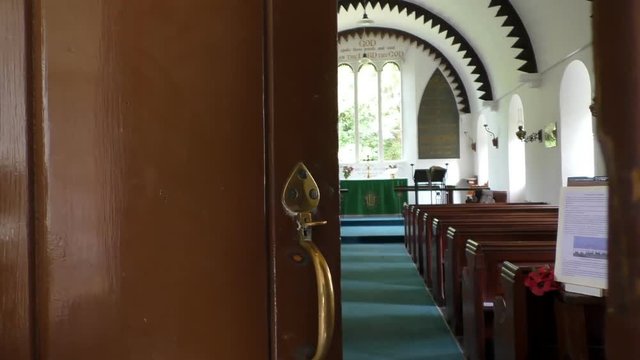 Handheld shot of hand opening wide old brown vintage door and entering small empty Christian church