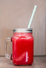 Watermelon smoothie in a mason jar with blue top on wooden background