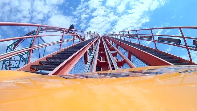 Roller coast heading up hill toward blue and cloudy sky.