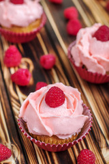 Cupcakes with pink cream and fresh raspberries on a brown wooden table. Close up.