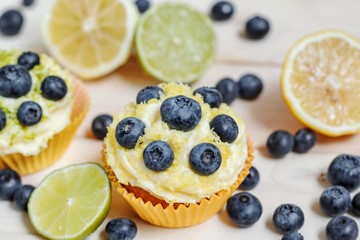 Blueberry cupcakes with butter cream on white wooden table, slice of lemon and lime, selective focus, close up.