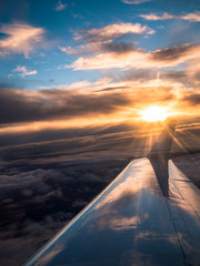 View from the airplane on the wing against the backdrop of a sunset with clouds and blue sky