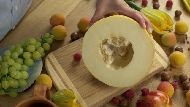 Cleaning of melon seeds. Cleaning a large metal spoon melon. Light wooden board. Green grapes and yellow flowers. Fruits and berries on a wooden table.