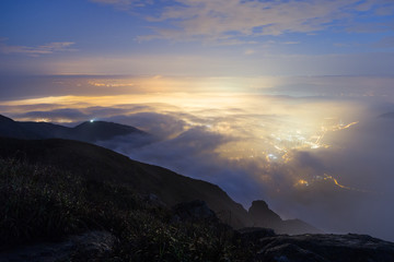 Lights of Tung Chung New Town below clouds on Lantau Island, viewed from the Lantau Peak (the 2nd highest peak in Hong Kong, China) at night.