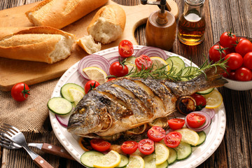 Grilled fish with baguette and vegetables on the plate