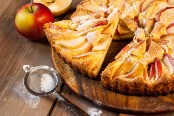 Traditional apple pie on a wooden table, with apple and powdered sugar