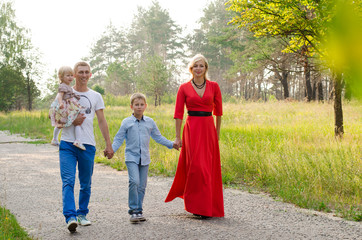 Naklejka na ściany i meble Big happy family walking on the road in the park. Father, mother, son, daughter and baby holding hands and going together. Rear view. Family Ties concept. 