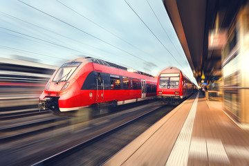 Naklejka premium Nowoczesne szybkie pociągi pasażerskie czerwone o zachodzie słońca Stacja kolejowa
