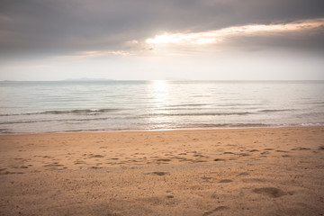 Tranquil sea at deserted sunset beach in soft tones with sunlight shining through the clouds