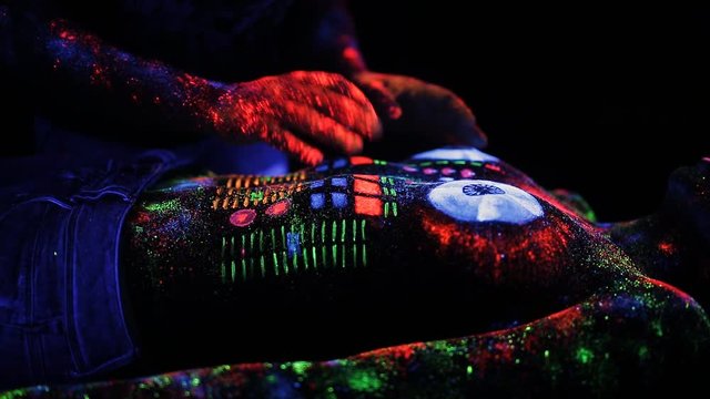 Hands DJ govern painted fluorescent powder on the body of a naked girl decks