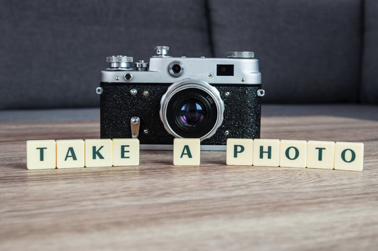 Stary aparat fotograficzny ustawiony na stole z literami układającymi się w napis zrób zdjęcie