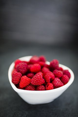 Fresh raspberries in bowl on dark background with space for text.