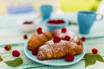 Delicious croissants and ripe raspberries on wooden table in the garden.
