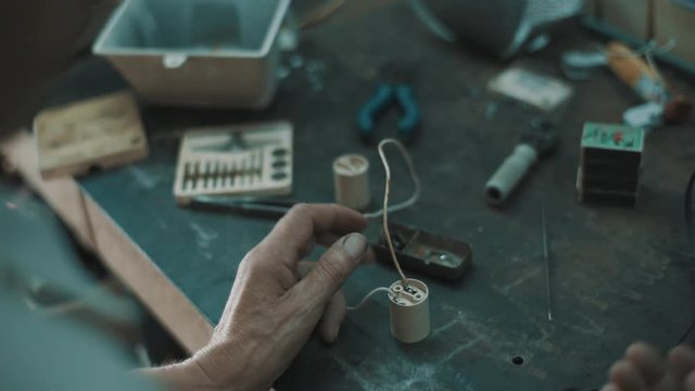Back view of elderly man in glasses working with electric object at table in workshop