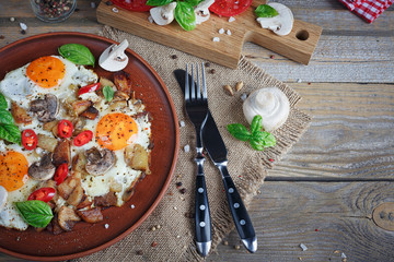 Fried eggs with mushrooms, tomatoes and basil on rustic wooden t