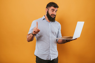 portrait of handsome smiling man isolated on yellow studio background posing to the camera and making funny faces, got idea, pointing to the monitor working on laptop computer