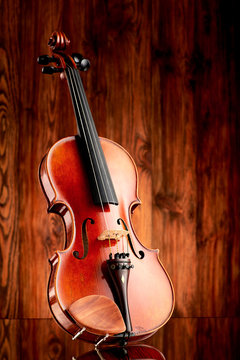 Close up of a violin on glass surface and wooden background