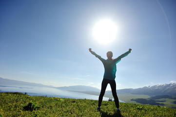 successful young woman open arms on sunrise mountain peak