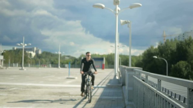 Male Cyclist Riding Down The Street And Stopped Because Of A Call To Teleofon. He Takes The Phone Out Of The Bag And Answers. Beautiful Sky Before A Storm On The Background