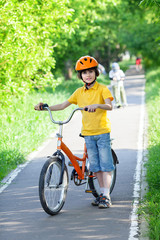 A young boy is standing at bike in city park in summer day