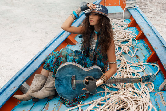 Atrractive young hippie woman with guitar sitting in old boat